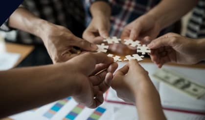 Team members joining puzzle pieces together over a desk